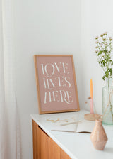 Cuadro decorativo de estilo minimalista y nórdico colocado en salón, frase tipográfica romántica en rosa empolvado, modelo Love Lives Here