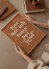 Gerahmtes Wandbild mit dekorativem Spruch love her, but leave her wild in weißen Buchstaben auf erdbraunem Hintergrund, organischen beigen Formen und modernem Schriftstil. Erhältlich auf kudeko.com