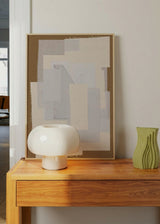 Quadro emoldurado com colagem têxtil de recortes retangulares sobrepostos em bege, cru, cinza-pérola e branco partido, num estilo abstrato sóbrio. Disponível em kudeko.com