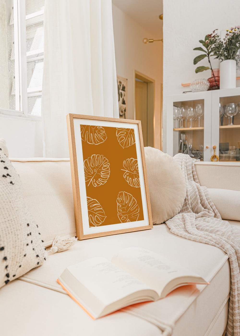 Quadro emoldurado com folhas tropicais monstera em contornos brancos sobre fundo terracota, composição botânica limpa de estilo minimalista, com tons terra e presença natural. Disponível em kudeko.com