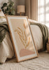 Gerahmtes Wandbild mit stilisiertem Blattzweig in ockerfarbener Linie, beigem Hintergrund, organischen Formen in Sand und Altrosa, im minimalistischen natürlichen Stil. Erhältlich auf kudeko.com