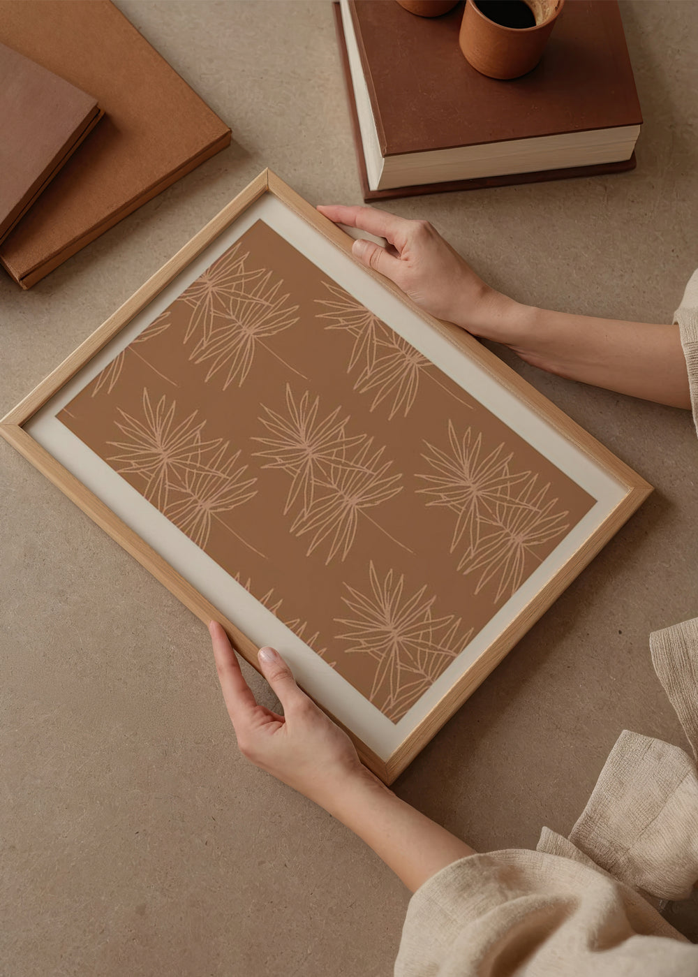 Quadro com folhas botânicas finas e ramos delineados em bege sobre fundo terracota quente, num estilo floral limpo e natural. Disponível em kudeko.com