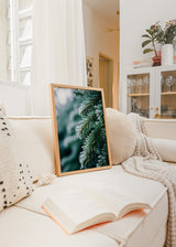 Wandbild mit bereiften Tannenzweigen, grünen Nadeln, weißen eisigen Details, verschwommenem Hintergrund in kühlen Tönen und fotografischem Stil. Erhältlich auf kudeko.com