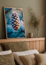 Wandbild mit verschneitem Tannenzapfen zwischen Kiefernzweigen, in Eisblau, frostigem Weiß, warmem Braun und natürlichem fotografischem Stil. Erhältlich auf kudeko.com