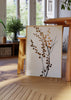Quadro emoldurado com ramos botânicos pretos, pequenas folhas redondas em dourado acobreado, fundo claro e estilo minimalista para decoração de parede. Disponível em kudeko.com