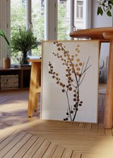 Quadro emoldurado com ramos botânicos pretos, pequenas folhas redondas em dourado acobreado, fundo claro e estilo minimalista para decoração de parede. Disponível em kudeko.com