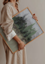 Wandbild mit nebliger Landschaft, verschwommenen Bäumen am Wasser, in Blaugrau, sanftem Grün, Beige und Schwarz, im Natur- und Landschaftsstil gerahmt. Erhältlich auf kudeko.com