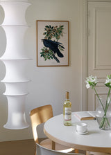 Tableau encadré avec corbeau noir posé sur une branche, feuilles vertes, fruits bruns, fond clair et composition botanique de style vintage. Disponible sur kudeko.com