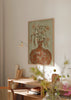 Dekoratives Wandbild im organischen Stil mit Illustration, in einem Wohnzimmer platziert, Terrakotta-Vase mit zarten Blumen, Modell Terracotta Vase Blossoms. Erhältlich auf kudeko.com