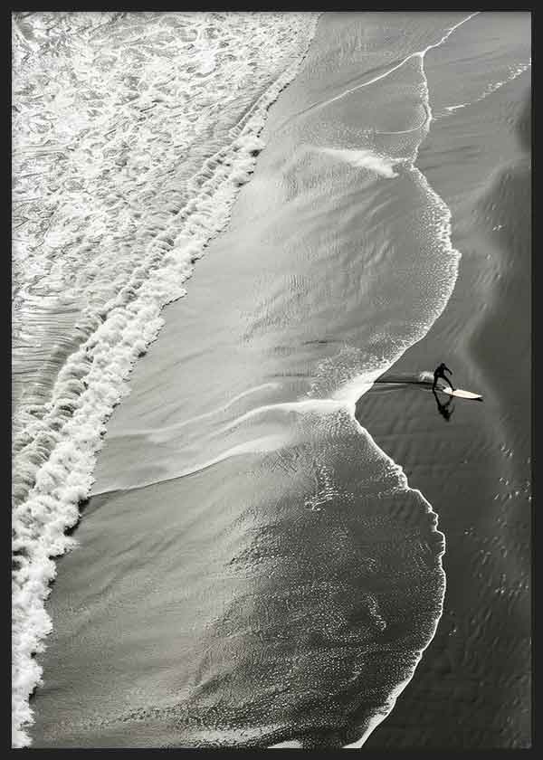 Quadro com vista aérea da rebentação branca sobre areia escura, surfista solitário, tons de cinzento preto e branco, estilo fotográfico contemporâneo. Disponível em kudeko.com