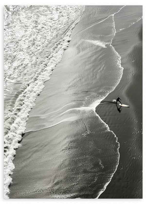 Quadro com vista aérea da rebentação branca sobre areia escura, surfista solitário, tons de cinzento preto e branco, estilo fotográfico contemporâneo. Disponível em kudeko.com