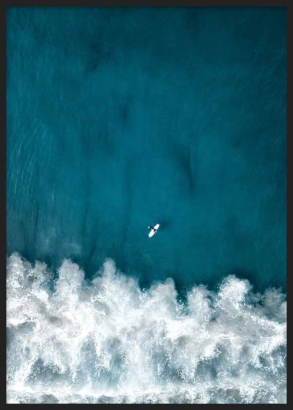 Cuadro de vista aérea del mar azul turquesa con olas de espuma blanca y una pequeña tabla de surf, de estilo fotográfico. Disponible en kudeko.com