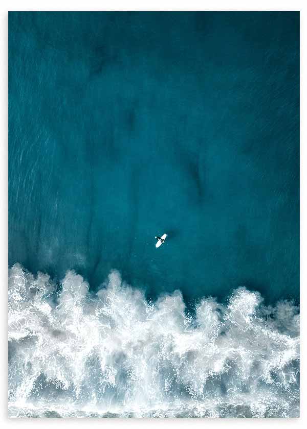 Cuadro de vista aérea del mar azul turquesa con olas de espuma blanca y una pequeña tabla de surf, de estilo fotográfico. Disponible en kudeko.com
