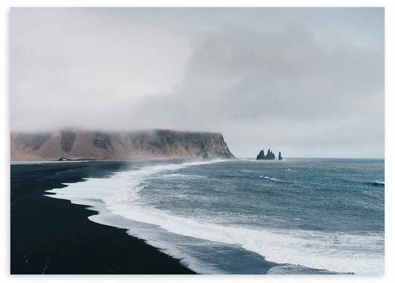 Cuadro horizontal de costa con playa de arena negra, mar azul grisáceo, espuma blanca, acantilados brumosos y rocas marinas, de estilo naturaleza y paisajes. Disponible en kudeko.com