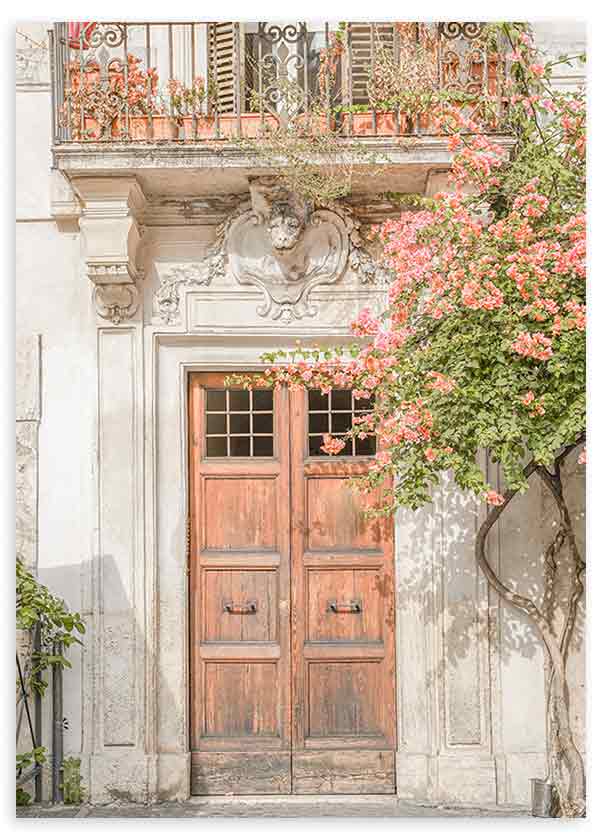 Wandbild mit klassischem Fassadeneingang, gealterter Holztür, ornamentalem Schmiedeeisenbalkon, rosa Blumen und grüner Rankpflanze in Cremefarben, urbaner mediterraner Stil. Erhältlich auf kudeko.com