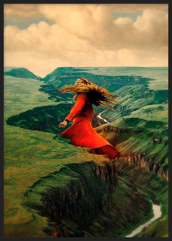 Gerahmtes Wandbild mit Frau mit wehenden Haaren, rotem Kleid auf Klippe, grüner Berglandschaft, türkisen Akzenten, beigem dramatischem Himmel und Illustrationsstil. Erhältlich auf kudeko.com
