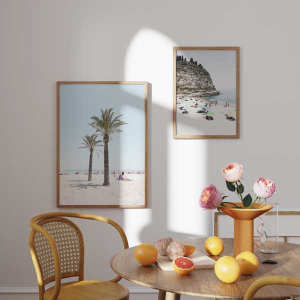 Conjunto de dois quadros com praia mediterrânica, palmeiras sobre areia clara, enseada com falésia rochosa, chapéus de sol em tons pastel, mar azul sereno e estilo fotográfico em bege, azul e verde. Disponível em kudeko.com