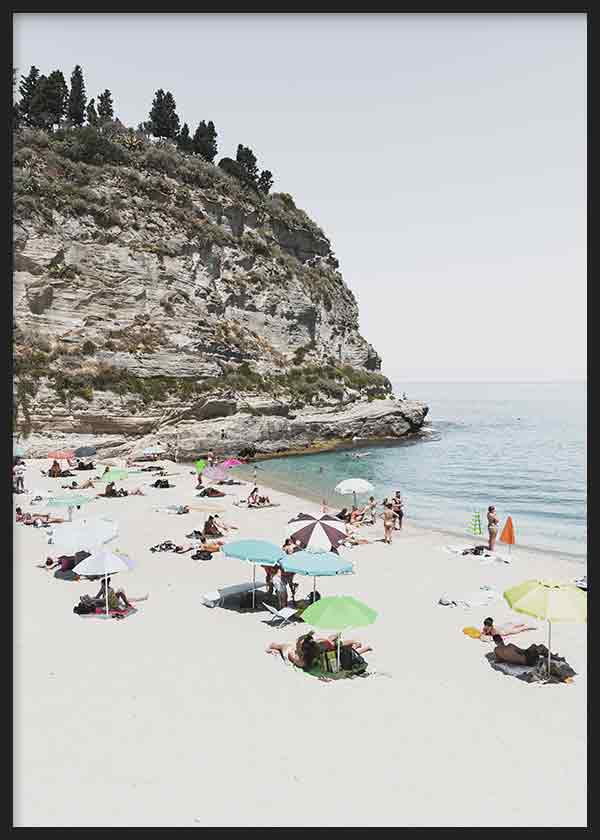 Cuadro de cala italiana con acantilado claro, arena blanca, mar azul sereno y sombrillas pastel, en estilo fotográfico. Disponible en kudeko.com