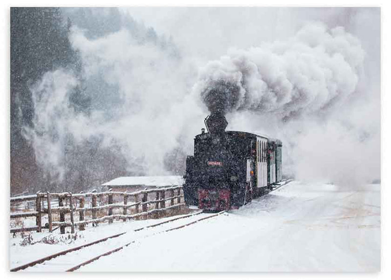 Cuadro horizontal de locomotora de vapor negra sobre vías nevadas, con humo blanco denso, paisaje invernal en grises y estilo fotográfico. Disponible en kudeko.com