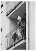 Cuadro de mujer en balcón de edificio urbano, en tonos blanco y negro, con barandillas metálicas, escena cotidiana y estilo fotográfico. Disponible en kudeko.com