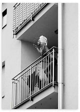 Cuadro de mujer en balcón de edificio urbano, en tonos blanco y negro, con barandillas metálicas, escena cotidiana y estilo fotográfico. Disponible en kudeko.com