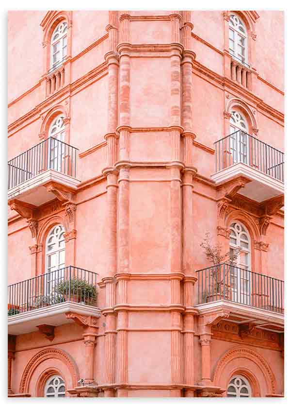 Tableau d’une façade classique rose pastel avec balcons en fer noir, fenêtres cintrées et détails architecturaux ornementés, dans un style photographique lumineux et équilibré. Disponible sur kudeko.com