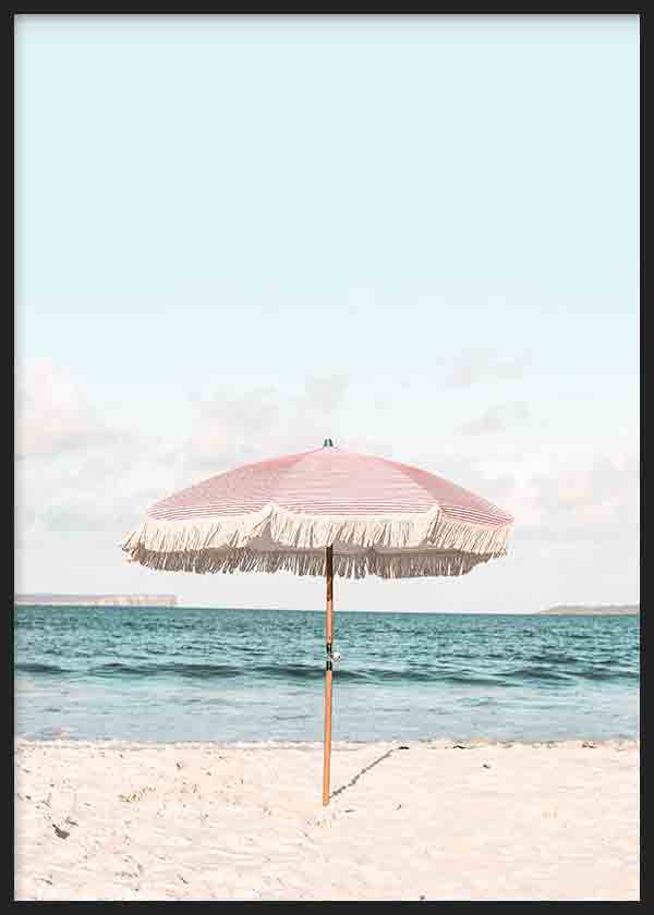 Cuadro de sombrilla rosa con flecos sobre playa de arena clara, mar azul sereno y cielo pastel, en estilo fotográfico. Disponible en kudeko.com