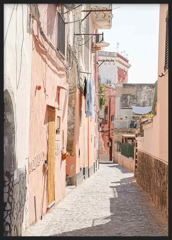 Cuadro de callejón mediterráneo con fachadas rosa, beige y terracota, suelo empedrado, balcones, ropa tendida y luz suave, de estilo fotográfico. Disponible en kudeko.com