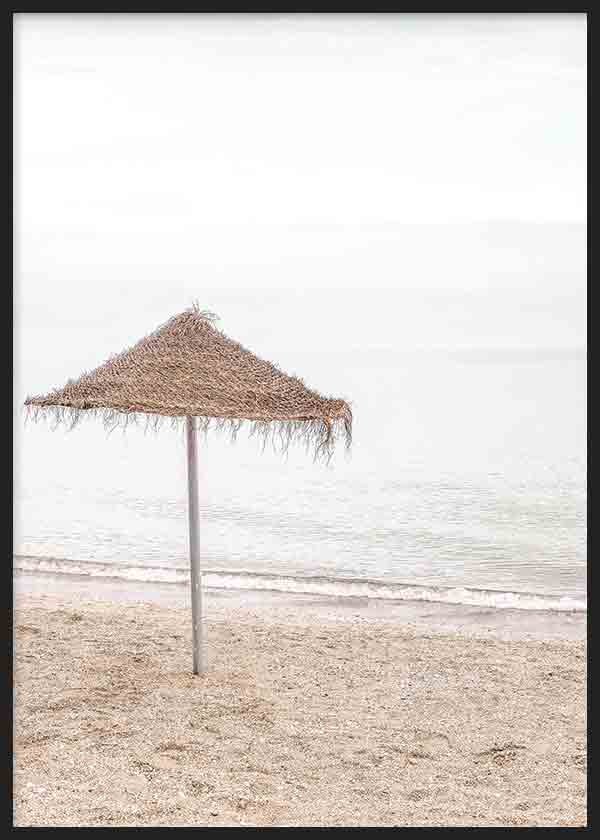 Cuadro de sombrilla de paja solitaria en la playa, con arena clara, mar en tonos beige y gris suave, y estilo fotográfico sereno. Disponible en kudeko.com