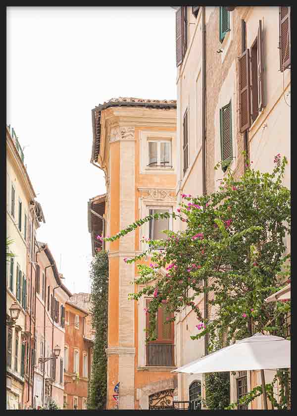 Quadro emoldurado de rua romana com fachadas em creme, pêssego e areia, portadas escuras, varandas, vegetação verde, flores fúcsia e estilo urbano mediterrânico. Disponível em kudeko.com