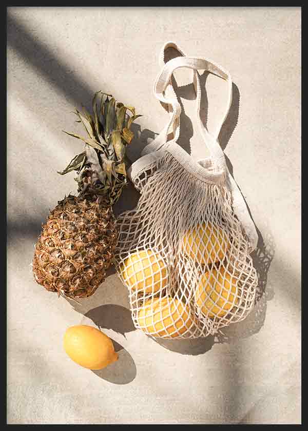 Cuadro de piña y limones amarillos en bolsa de malla beige, sobre fondo claro con sombras suaves, de estilo fotográfico. Disponible en kudeko.com