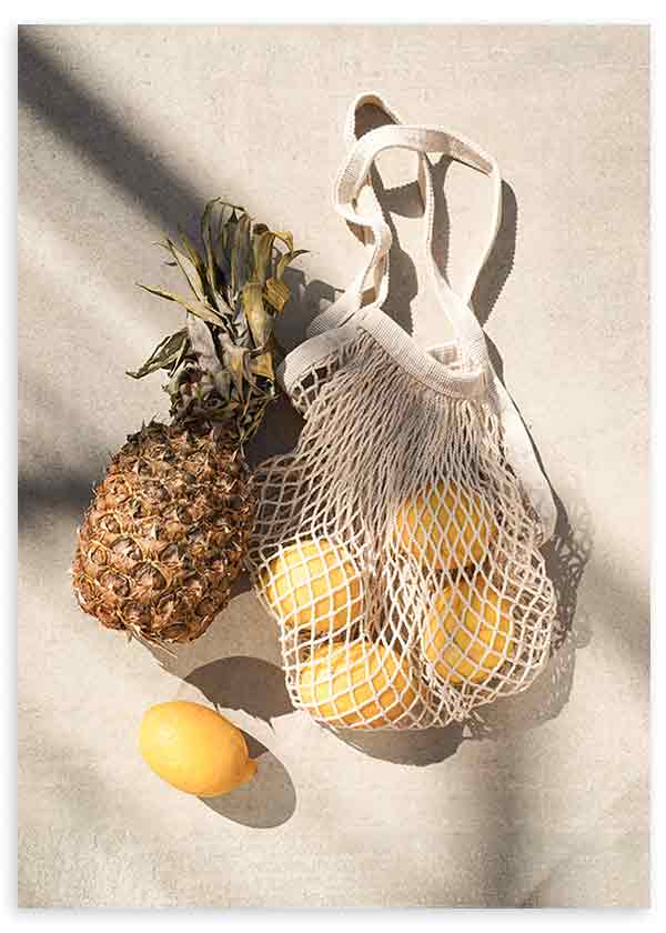 Cuadro de piña y limones amarillos en bolsa de malla beige, sobre fondo claro con sombras suaves, de estilo fotográfico. Disponible en kudeko.com