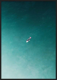 Tableau représentant un surfeur solitaire sur une planche blanche, au cœur d’une mer turquoise et bleu-vert, dans une composition aérienne au style photographique épuré. Disponible sur kudeko.com