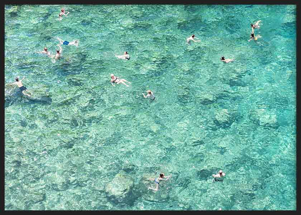 Cuadro horizontal de personas nadando en mar cristalino turquesa y aguamarina, con fondo rocoso visible y estilo fotográfico de aire veraniego. Disponible en kudeko.com