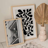 Cuadro de mujer en balcón de edificio urbano, en tonos blanco y negro, con barandillas metálicas, escena cotidiana y estilo fotográfico. Disponible en kudeko.com