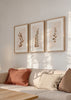 Set aus drei Wandbildern mit stilisierten botanischen Blättern in Kupfer, Braun und hellem Beige, florale Komposition auf sanftem Hintergrund im nordischen Stil als gerahmte Wanddekoration. Erhältlich auf kudeko.com