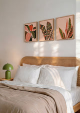Set aus drei Wandbildern mit langen und breiten tropischen Blättern in Korallenrot, Olivgrün, Zartrosa und Schwarz, als botanische Komposition im floralen Stil auf hellem Hintergrund. Erhältlich auf kudeko.com