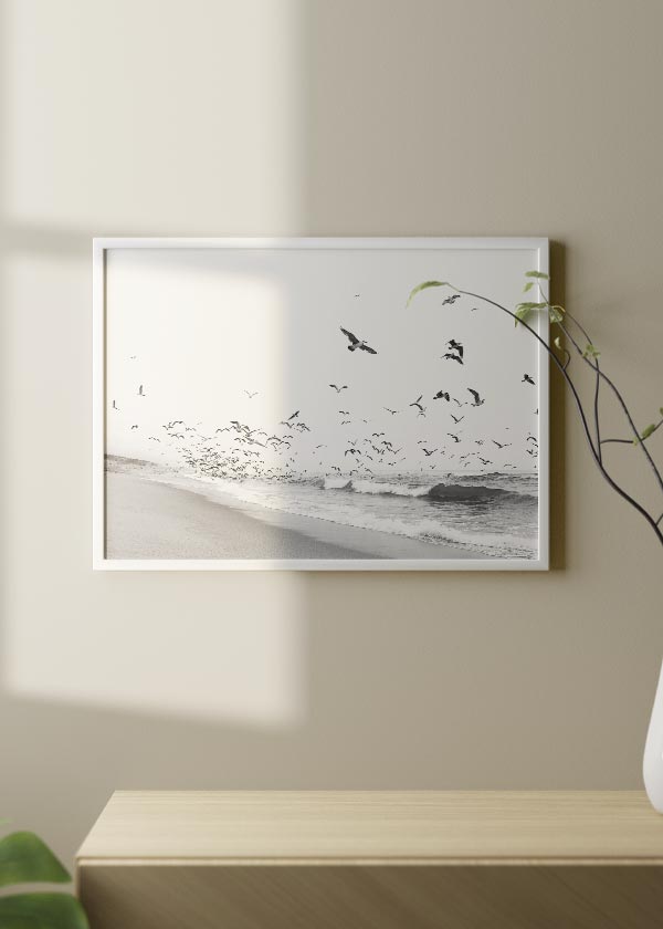 Cuadro horizontal de playa en blanco y negro con bandada de aves sobre el mar, arena suave, olas ligeras y composición fotográfica serena. Disponible en kudeko.com