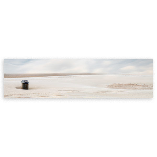 Cuadro horizontal de una papelera solitaria en una playa desierta de arena beige y cielo gris suave, en estilo fotográfico. Disponible en kudeko.com