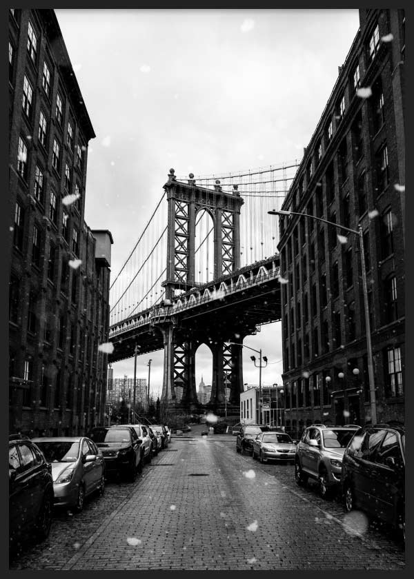 Cuadro del puente de Manhattan entre edificios de ladrillo, calle adoquinada, coches aparcados, copos de nieve y tonos blanco y negro, de estilo fotográfico. Disponible en kudeko.com