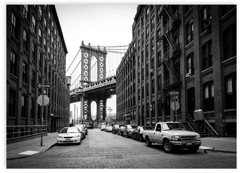 Quadro horizontal de rua empedrada em Brooklyn com a ponte de Manhattan, edifícios de tijolo, carros estacionados, tons a preto e branco e estilo urbano fotográfico. Disponível em kudeko.com