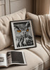 Quadro emoldurado com coruja em primeiro plano, plumagem branca, preta e cinzenta, olhos alaranjados intensos, estilo animal elegante e fundo escuro contrastante. Disponível em kudeko.com