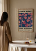 Quadro emoldurado com flores abstratas de formas orgânicas em tons rosa sobre fundo azul profundo, tipografia preta e estilo floral contemporâneo para parede. Disponível em kudeko.com