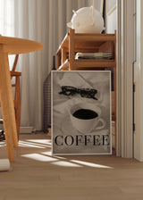 Gerahmtes Wandbild mit schwarzem Kaffee auf weißer Untertasse, offenem Buch, dunkler Brille, hellen Stoffen, in Weiß, Schwarz und Grau, fotografischer Stil. Erhältlich auf kudeko.com