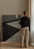 Quadro de cena arquitetónica a preto e branco com sombras diagonais, chão de betão texturado, figura humana distante e estilo fotográfico contemporâneo. Disponível em kudeko.com