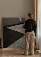 Quadro de cena arquitetónica a preto e branco com sombras diagonais, chão de betão texturado, figura humana distante e estilo fotográfico contemporâneo. Disponível em kudeko.com
