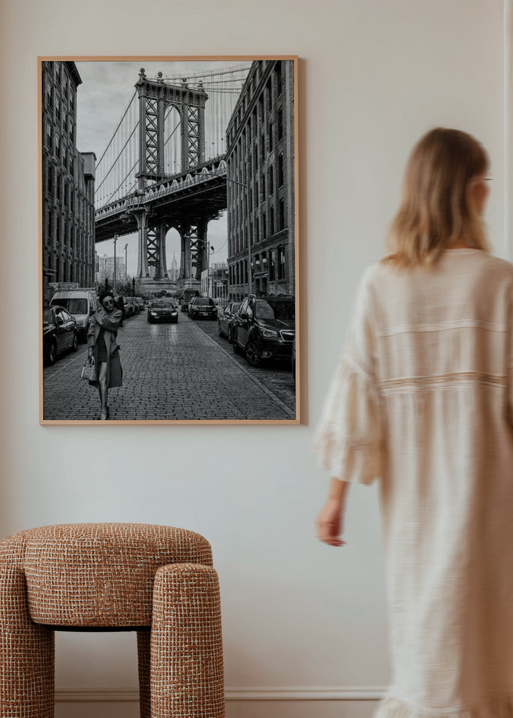 Wandbild einer urbanen Straße in Schwarz-Weiß mit großer Hängebrücke, Backsteingebäuden, parkenden Autos und weiblicher Figur im Vordergrund, im fotografischen filmischen Stil. Erhältlich auf kudeko.com