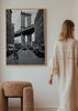Tableau d’une rue urbaine en noir et blanc avec grand pont suspendu, bâtiments en briques, voitures stationnées et silhouette féminine, dans un style photographique cinématographique. Disponible sur kudeko.com