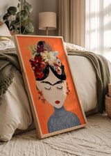 Quadro emoldurado com retrato feminino inspirado em Frida Kahlo, flores vermelhas brancas e rosa, fundo laranja e estilo de ilustração contemporânea para decoração de parede. Disponível em kudeko.com