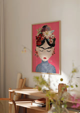 Quadro com retrato feminino inspirado em Frida, fundo rosa forte, flores em bordô, creme e verde, lábios vermelhos, expressão serena e estilo de ilustração decorativa. Disponível em kudeko.com